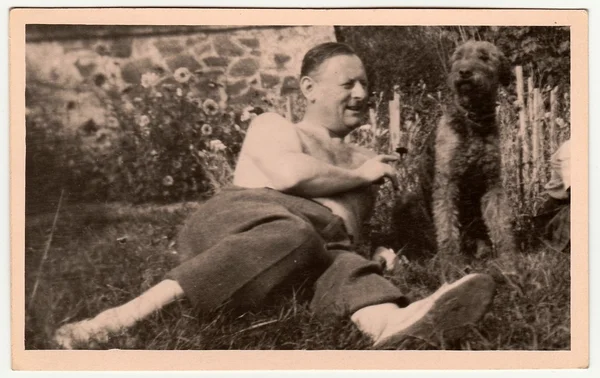 Vintage photo shows man with dog outdoors. Black & white antique photography.