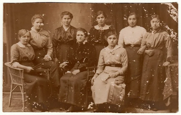 Vintage photo shows group of women pose at the photography studio. Black & white antique photography.