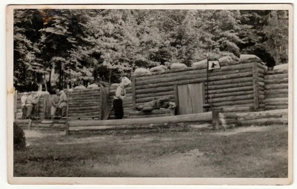 Vintage photo shows soldiers in front of log fortification. Black & white antique photography.