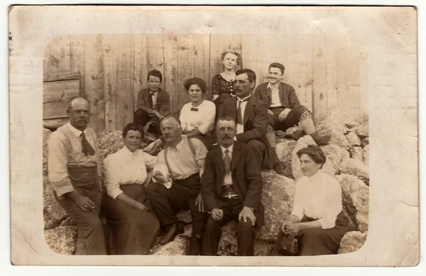 Vintage photo shows group of people sit in the back yard. Black & white antique photography.