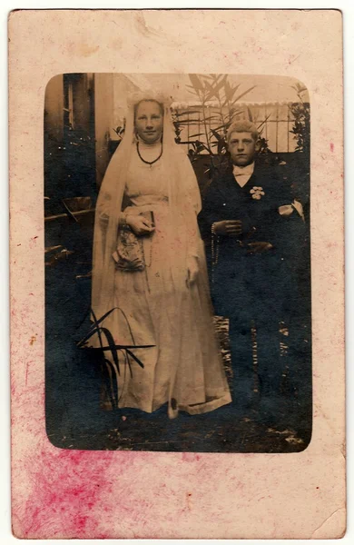 Vintage photo shows rural newlyweds pose outdoors. Black & white antique photography.