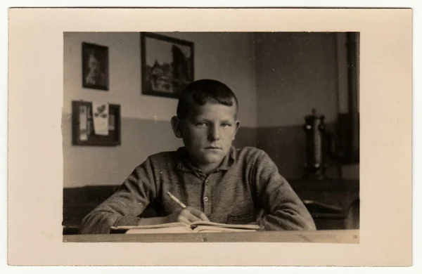 Vintage photo shows young boy (pupil, student) sits at the classroom. Black & white antique photography.
