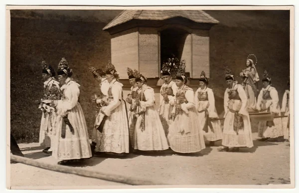Vintage photo shows young women during religion procession. Women wear folk costums. Black & white antique photography.