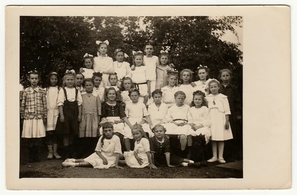 Vintage photo shows group of girls (schoolmates, pupils) pose outdoors. Black & white antique photography.