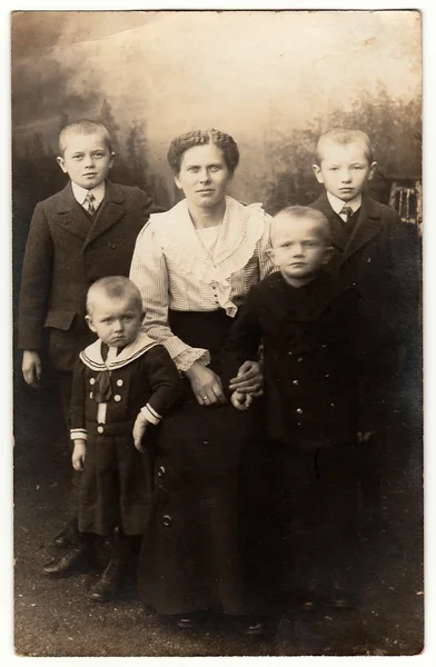 Vintage photo shows mother and her four sons. One of them wears sailor costum. Black & white antique photography.