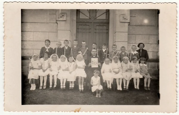 Vintage photo of children at the First Communion. On photography is a priest and female teacher (schoolmistress).