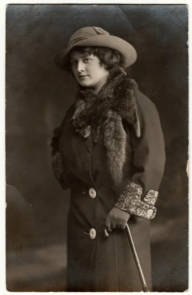 Vintage photo shows a young elegant woman wears hat, fur scarf and coat. Black & white studio photography.