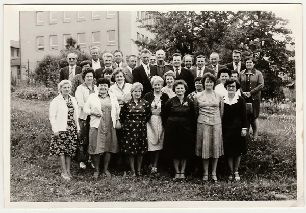 Retro photo shows group of people pose outdoors. Black & white vintage photography.