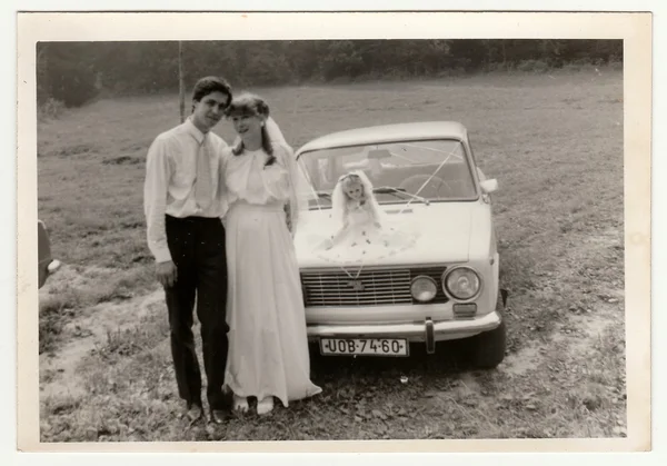 Retro photo shows newlyweds and wedding car. Black & white vintage photography.