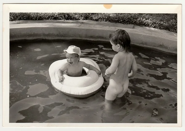 Retro photo shows children in the outdoor pool during summer time. Black & white vintage photography.