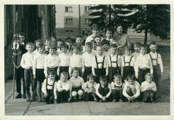 Retro photo shows small pupils and they female teachers (schoolmistresses) pose for photograper outside. Vintage black & white photography.