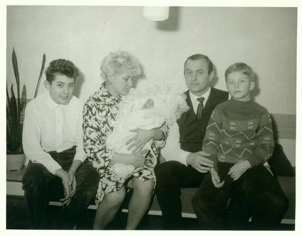 Retro photo shows family sits in the living room. Woman cradles newborn baby. Vintage black & white photography.