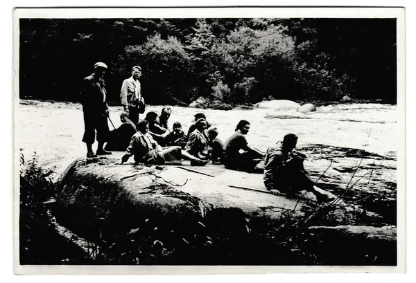 Retro photo shows tourists have a rest on the bank of the river. Black & white vintage photography.