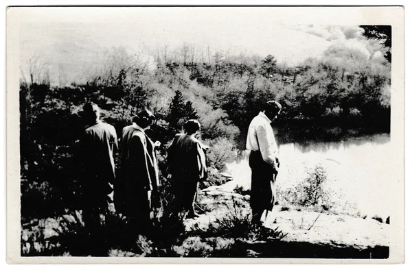 Retro photo shows tourists stand on the bank of the pond. Black & white vintage photography