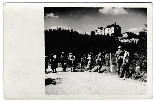 Retro photo shows tourists outside. The castle is on background. Vintage black & white photography.