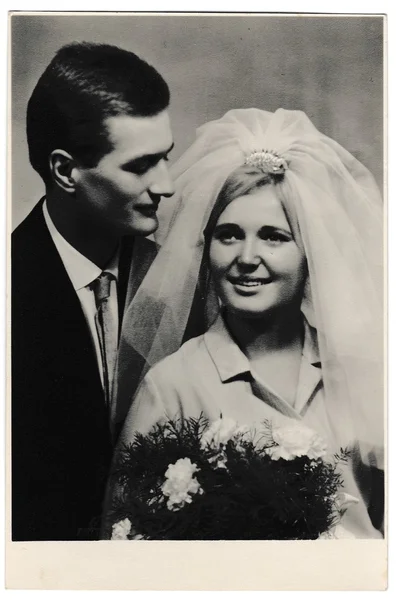 Retro photo shows bride wears a white veil and groom wears a dark suit.  Black & white vintage photography of wedding couple.