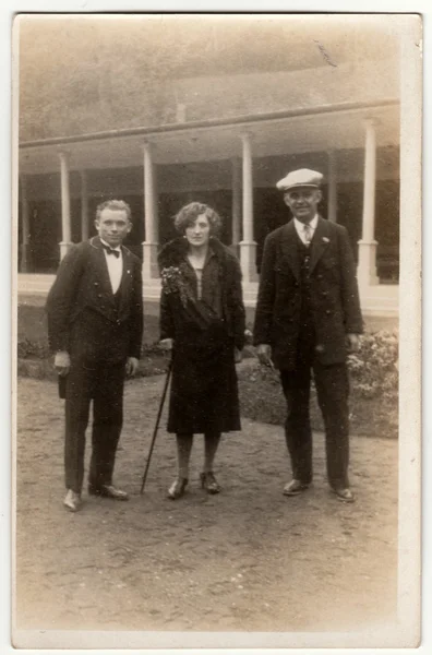 Vintage photo shows two men and woman pose outside. Original retro black & white photography.
