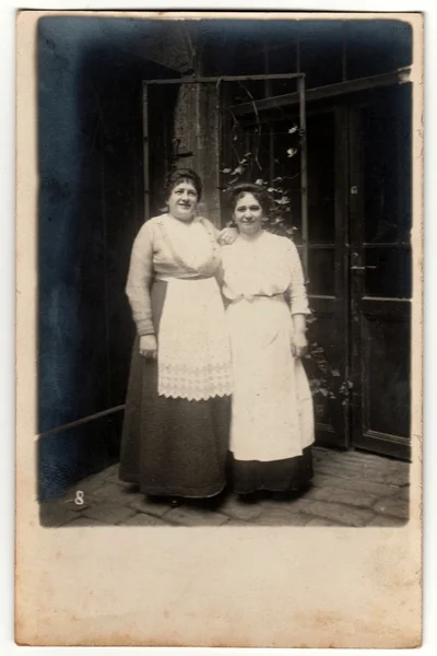 Vintage photo shows two housekeepers pose outside - in the backyard. Retro black & white photography.