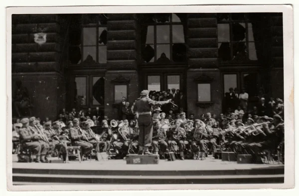 Vintage photo shows army orchestra plays outside. Retro black & white photography.