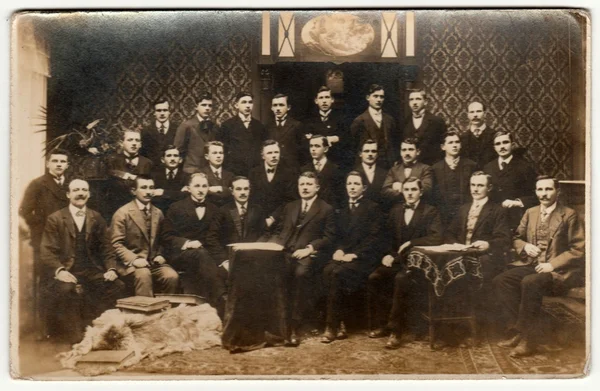 Vintage photo shows group of men poses in an elegant room. Black & white photography with sepia effect