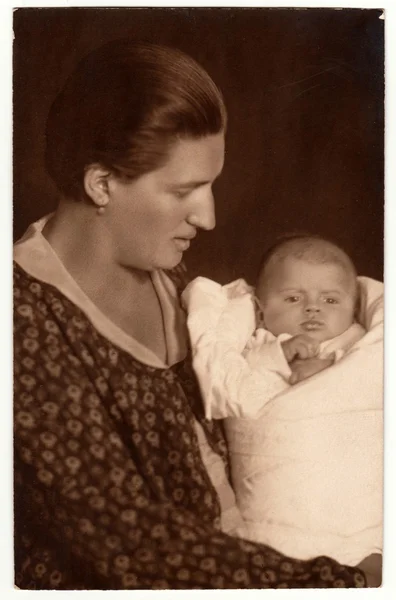 Vintage photo shows woman with baby (newborn) in swaddling clothes. Retro black & white studio photography.
