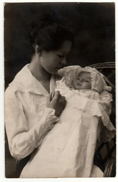 Vintage photo shows woman with baby (newborn) in swaddling clothes. Retro black & white studio photography.