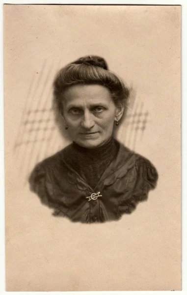 Vintage photo shows elderly woman - portrait in a photography studio. Woman with Edwardian hairstyle. Retro black & white studio photography with sepia effect. Head is drawn to body.