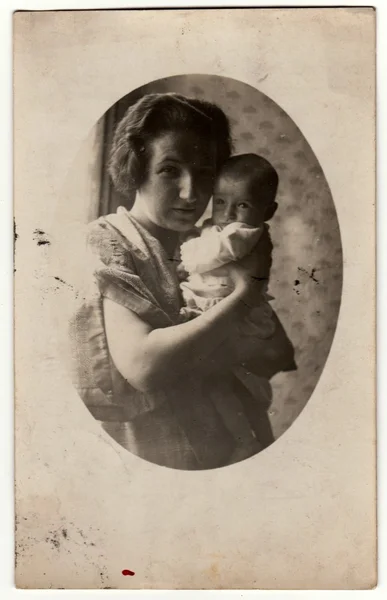 Vintage photo shows mother cradles a small baby. Retro black & white photography.