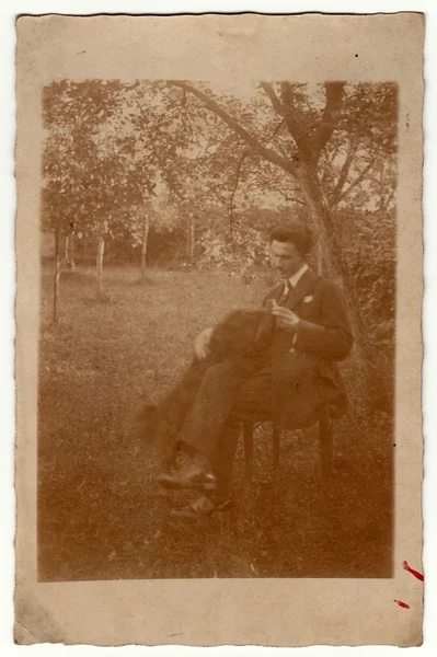 Vintage photo shows man sits on a chair in the garden. Retro black & white photography with sepia effect.