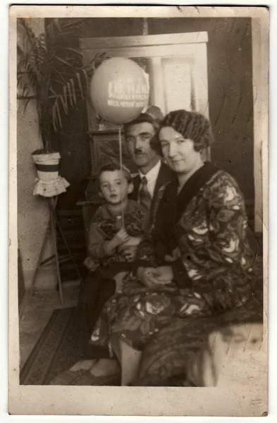 Vintage photo shows family in the living room. Boy holds air-ball (inflatable ball). Retro black & white photography.