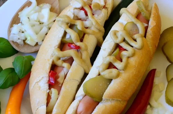 Hot dog with chilli, sport peppers, onion and cucumbers on white plate with wood background