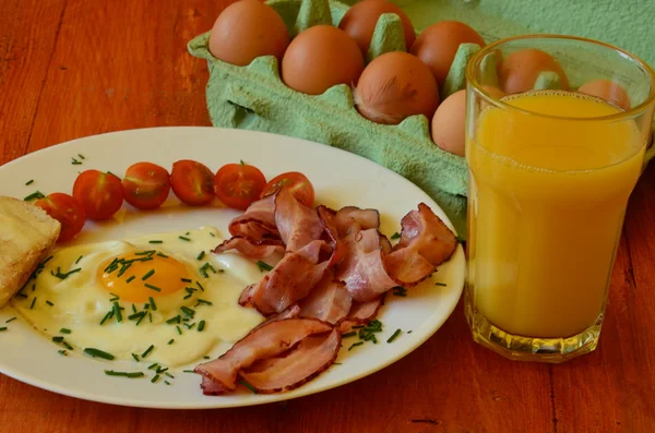 Sunny side up eggs with chives, cherry tomatoes and roasted bread with butter and the glass of orange juice on red background