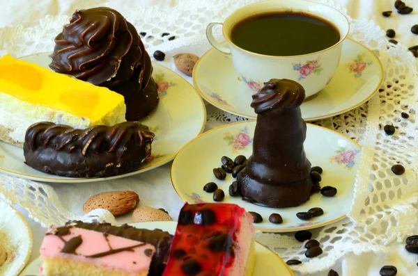 Desserts with cup of coffee, coffee beans and almonds on white tablecloth.