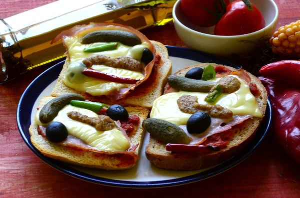 Baked bread with ham, cheese, mustard, gherkins and olives.