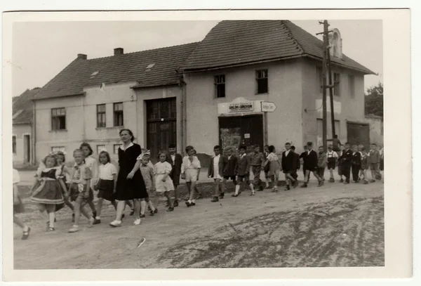Vintage photo shows female teacher with her pupils go for a walk.