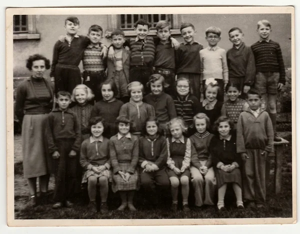 A vintage photo shows schoolmates with female teacher.