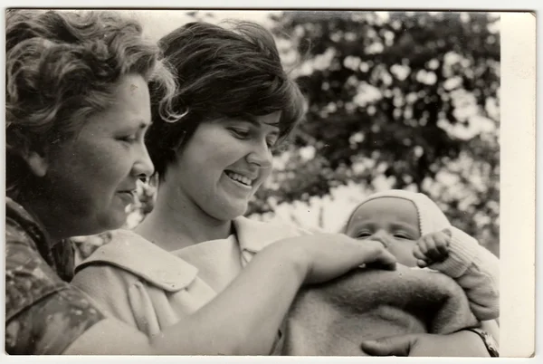 Vintage photo shows young woman cradles baby and its grandmother.