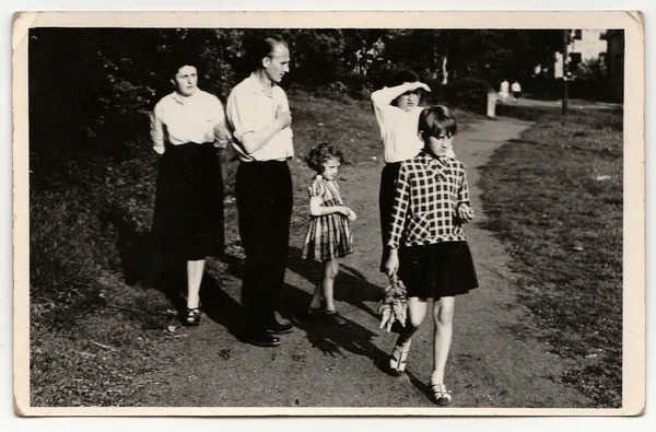 A vintage photo shows family goes for a  walk in the city park. Antique black & white photo.