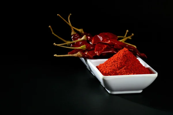 Chilly powder with red chilly in white plate, dried chillies on black background