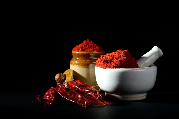 Red Chili Pepper powder in pestle with mortar and clay pot with Red Chili Peppers on black background