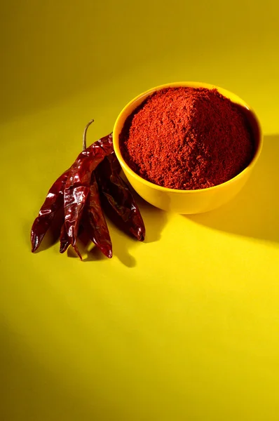 Chili powder in yellow bowl on yellow background. Red chilly pepper