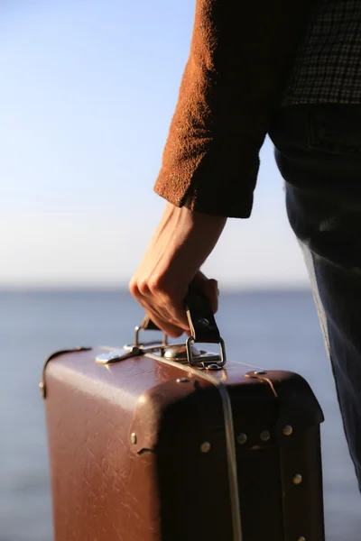 Luggage in a female hand on a background of the sea