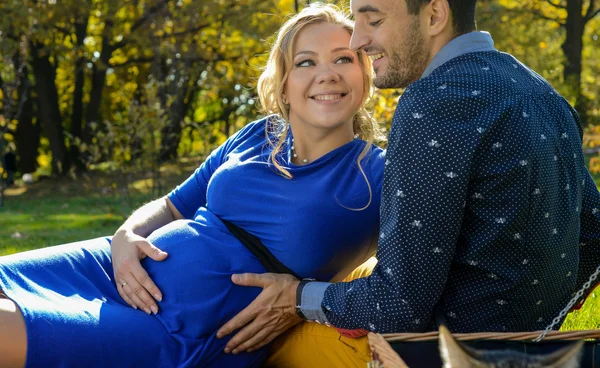 Happy parents expecting baby, touching belly, sitting on green grass