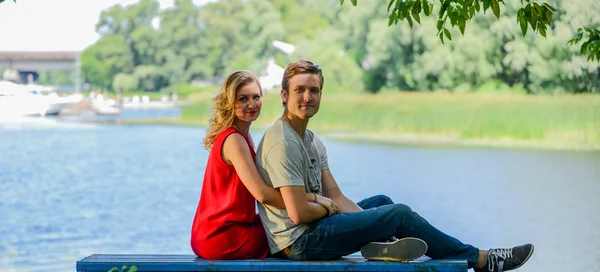 Young and happy couple sitting on the bench hugging. River background