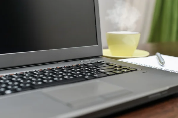 Laptop an address book, cup and pen on the table.