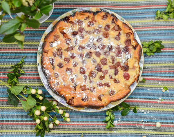 Cherry pie on the colorful tablecloth with green twig