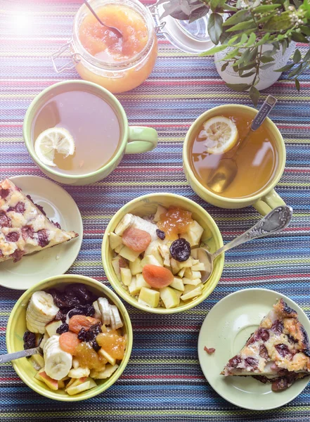 Breakfast with cereal mush, fruits, pie and tea. On the colorful tablecloth.