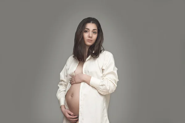 Young pregnant woman in white shirt holding her hands on belly