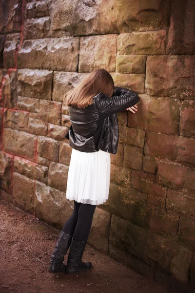 Back of a teenage girl leaning against a wall with her head in h