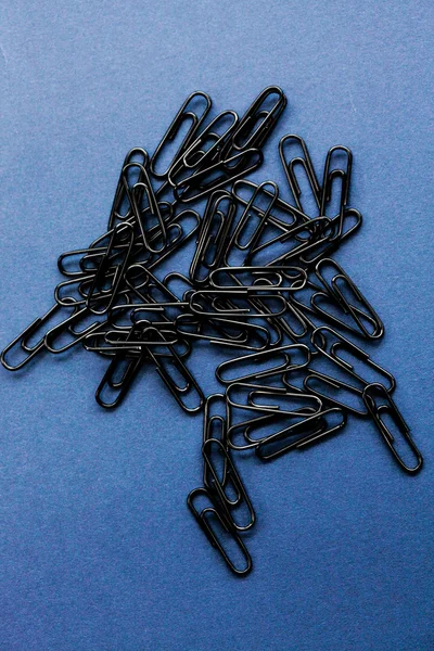 Close up of black paperclips on a plain background